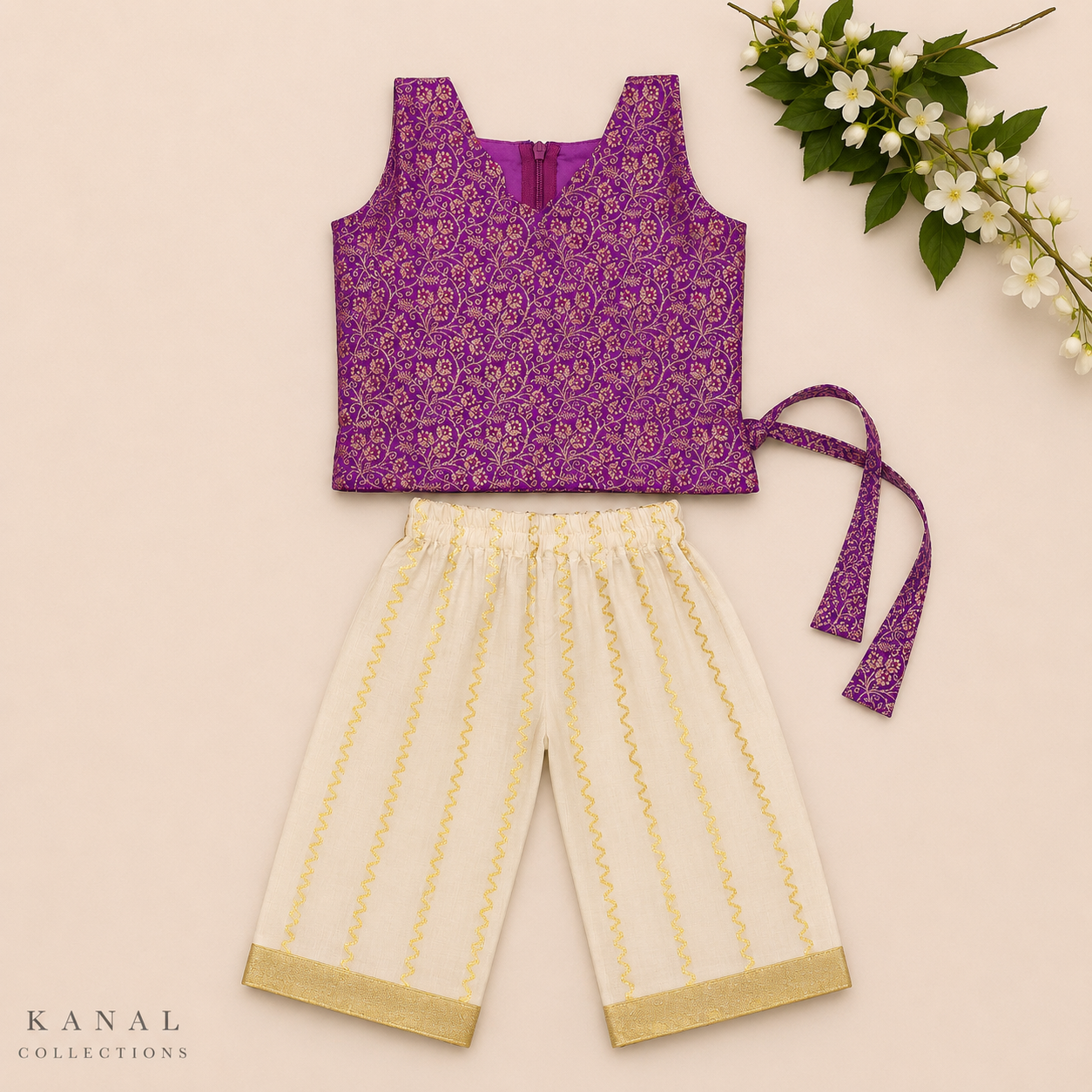 A two-piece children's outfit laid flat on a light beige background, featuring a sleeveless purple top with a gold floral pattern and matching purple tie, paired with cream-colored pants with gold vertical stripes and gold trim. White flowers are arranged in the top right corner, and the brand name 'KANAL COLLECTIONS' is visible in the bottom left.