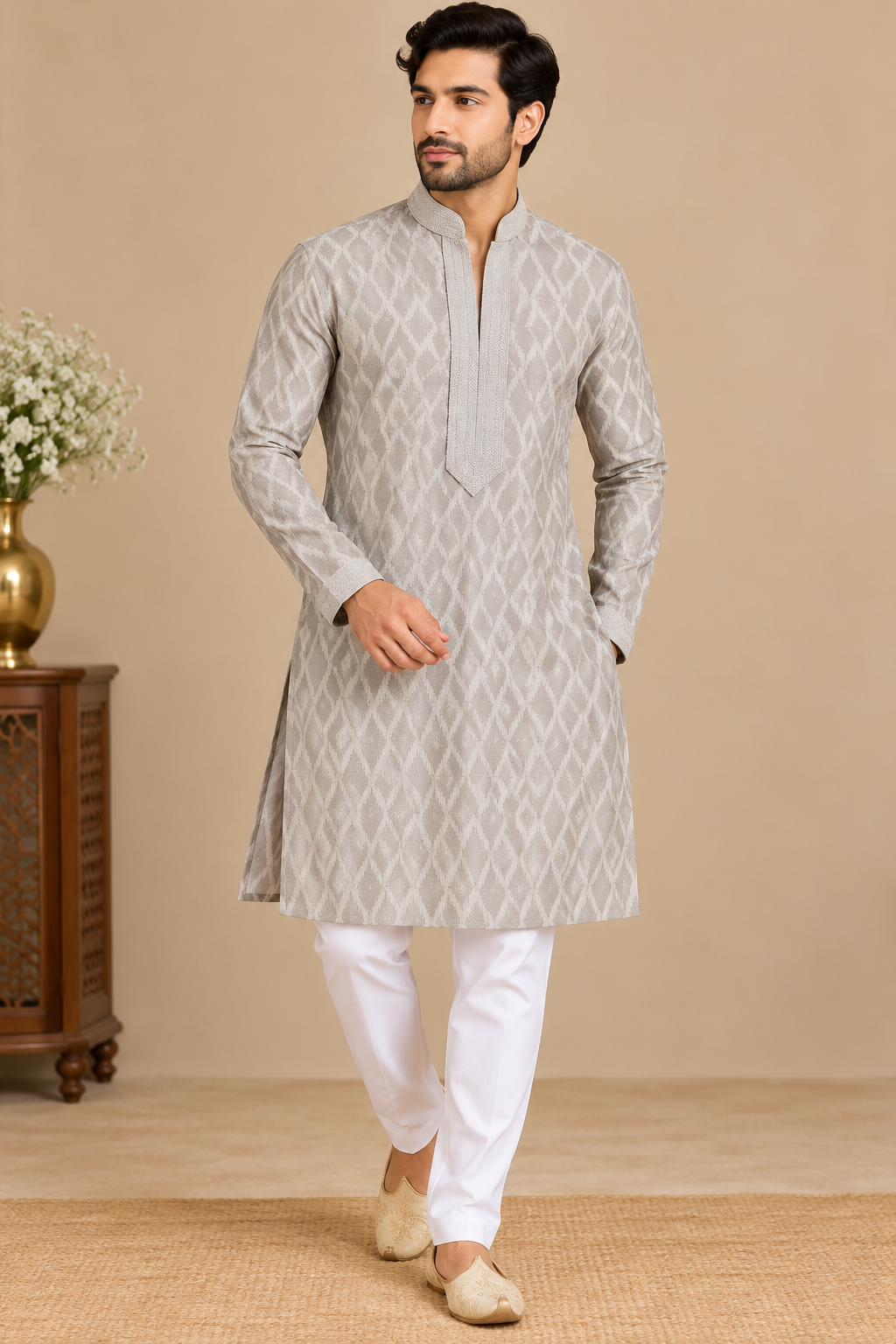 A man modeling a light gray long-sleeve kurta with a subtle geometric pattern, paired with white trousers and beige shoes, standing against a warm beige background.