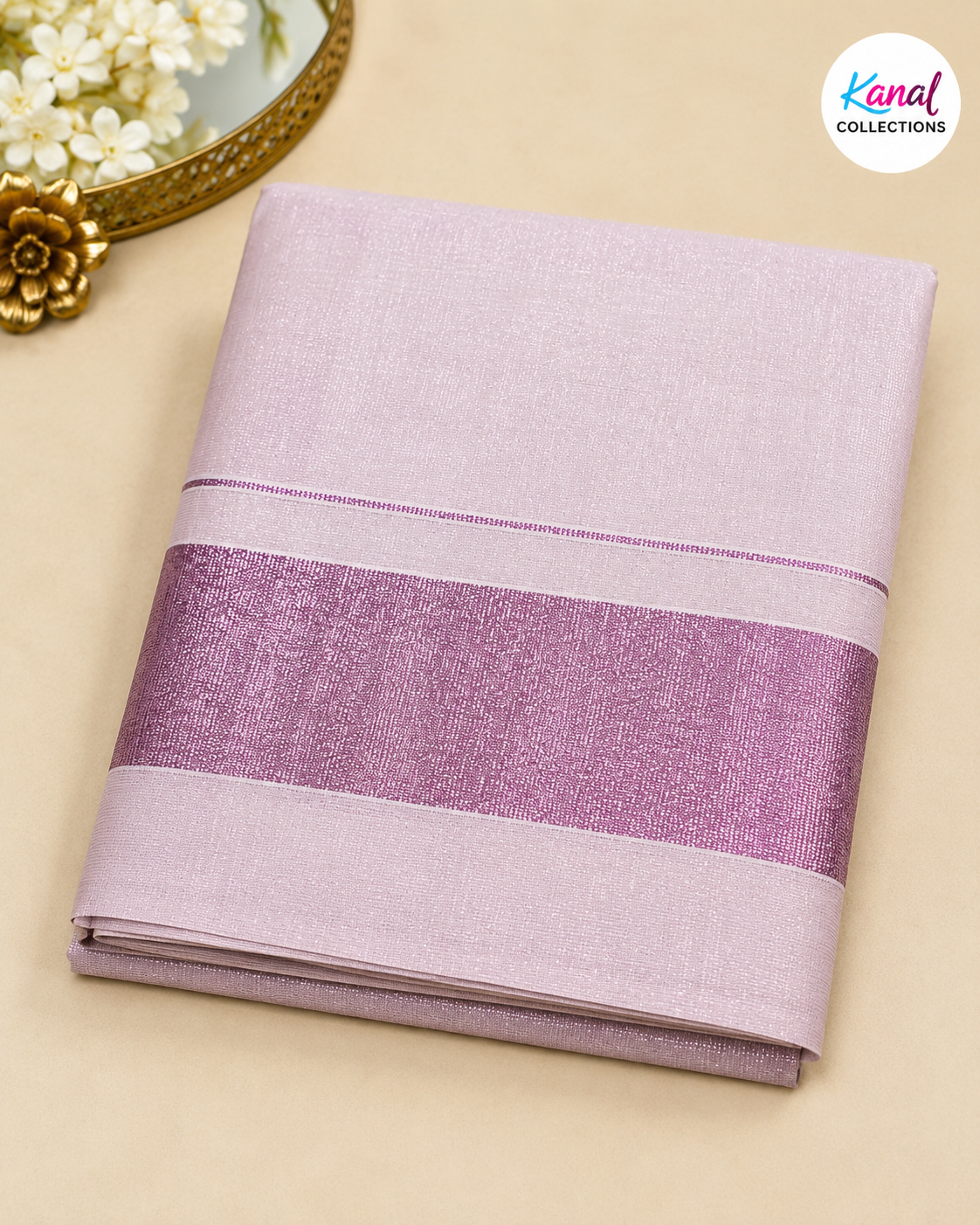 A folded light purple/lavender fabric item, likely a sari or textile, with a wide shimmering mauve-purple band across the middle, photographed on a beige surface with decorative flowers and a gold mirror edge in the corner. A 'Kanal Collections' logo appears in the top right.