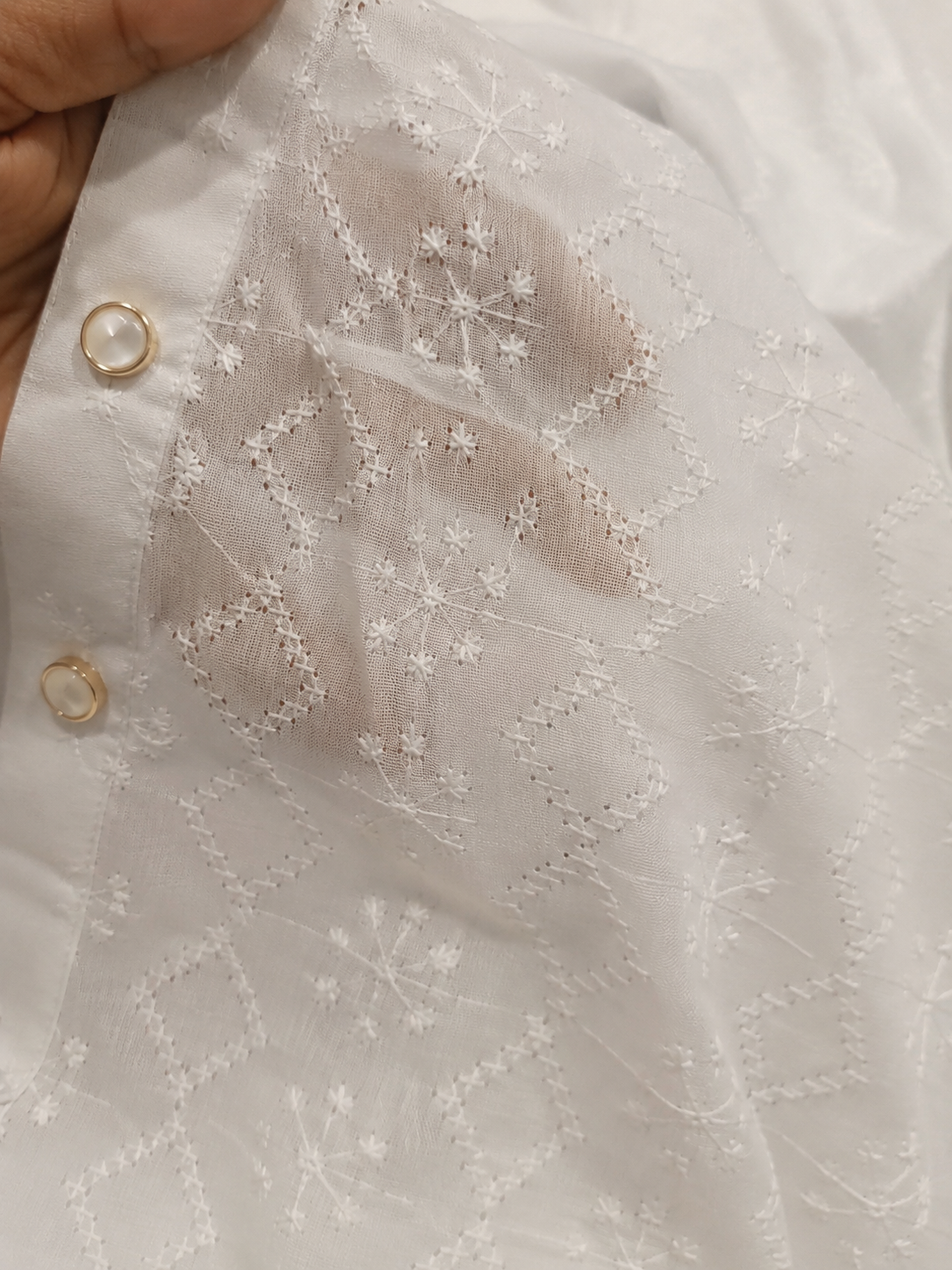Close-up detail of the premium white cotton fabric showing the intricate tone-on-tone geometric starburst embroidery and gold-trimmed buttons on a boys kurta.